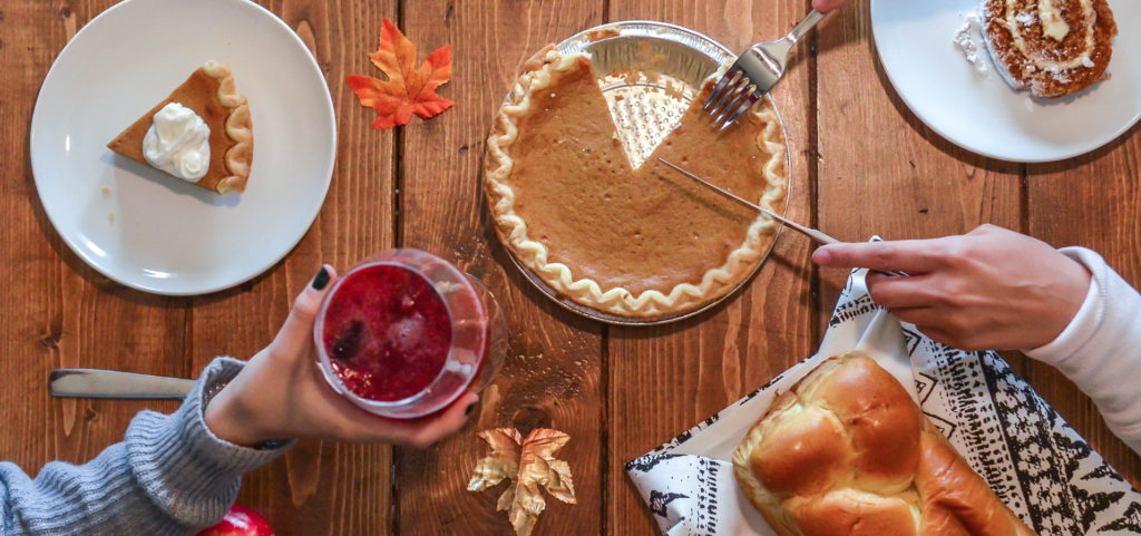 Thanksgiving table display of pie, wine, fresh bread and people clinking their glasses above the display of food