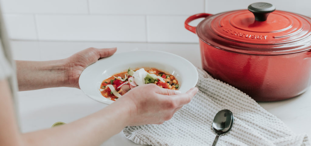 Women holding a bowl of vegetable soup over top of a stove top